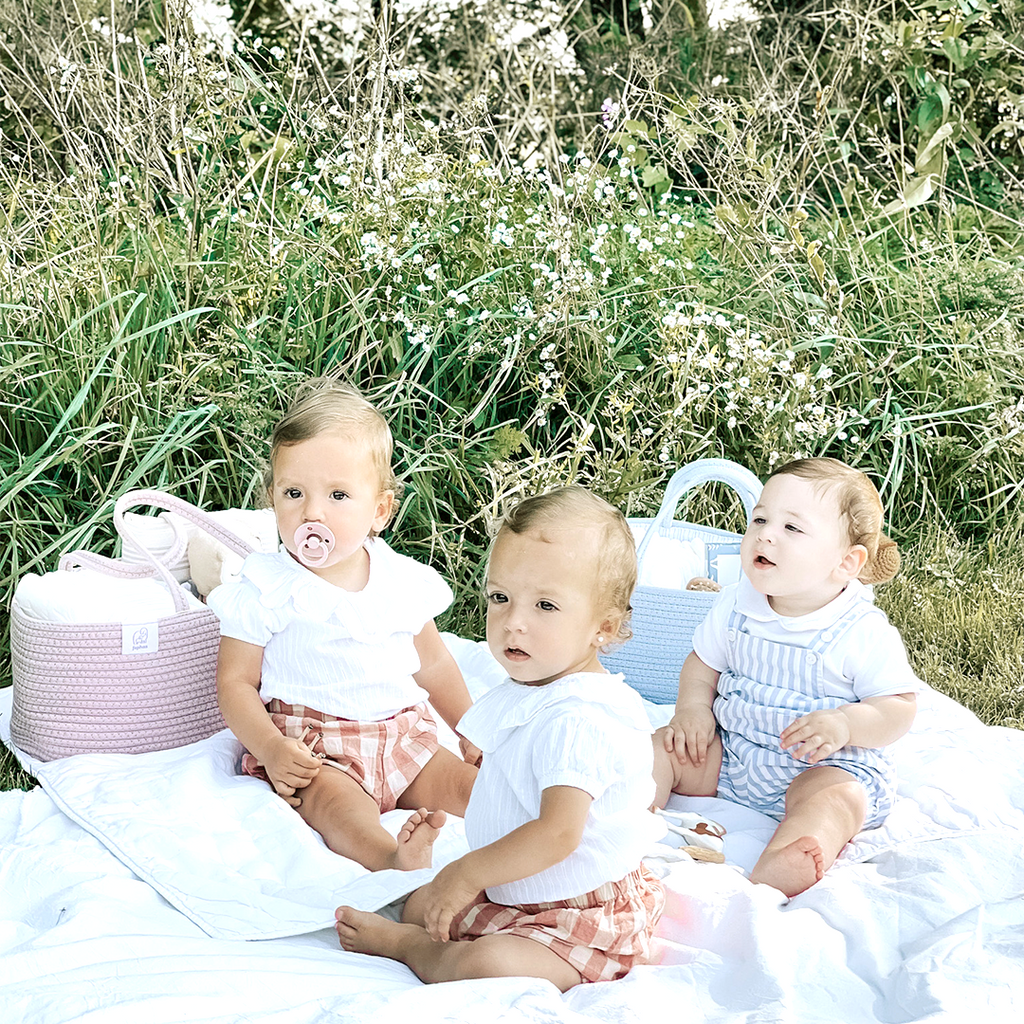 Babies sitting on playmat next to two diaper caddies